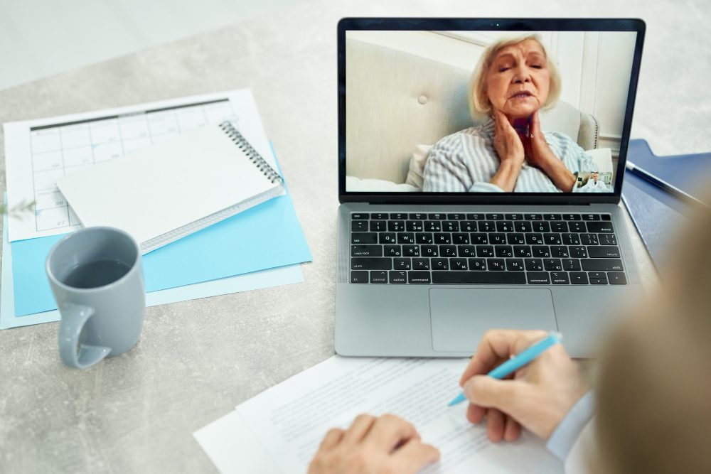 Klinik psikolog, dizüstü bilgisayar üzerinden online görüşme yapan yaşlı danışanla konuşurken not alıyor